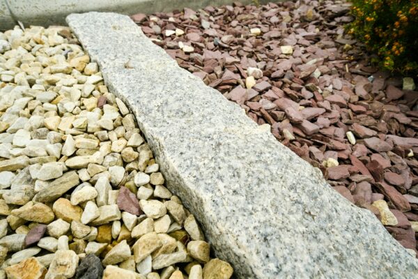 A close-up view of a curved granite border separating two areas of landscaping rocks, with white and cream-colored stones on one side and red and brown stones on the other.