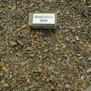 A concrete block with the label "BRONZE MULCH 40MM" sits on a bed of small, multicolored stones and fragments.