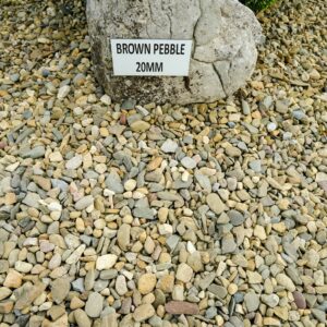 An assortment of multicolored pebbles on the ground with a large rock to the left bearing a sign that reads "BROWN PEBBLE 20MM."