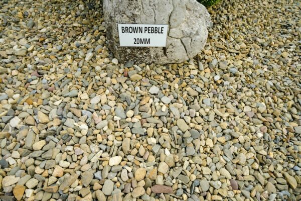 An assortment of multicolored pebbles on the ground with a large rock to the left bearing a sign that reads "BROWN PEBBLE 20MM."