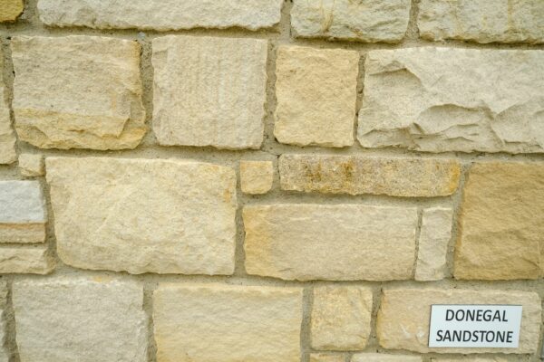 A close-up of a wall made from rectangular blocks of Donegal sandstone, with a label stating "DONEGAL SANDSTONE" attached to the wall.