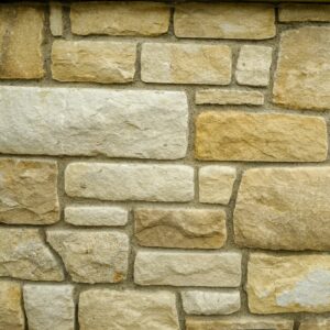 A wall of tumbled Donegal sandstone blocks in various sizes and shades of beige, with a sign in the upper left corner labeling the stone type.