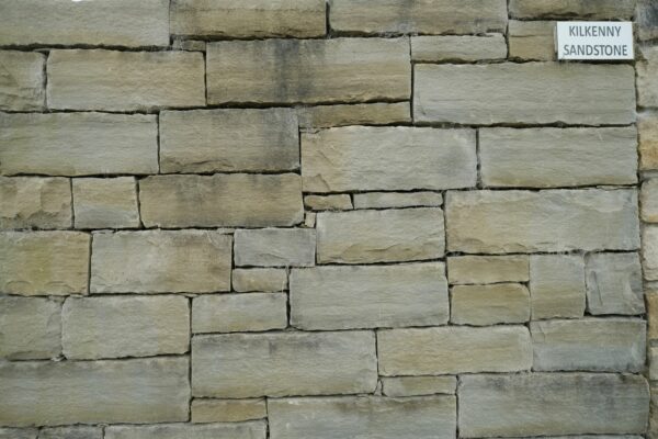 A textured wall made of Kilkenny sandstone blocks neatly arranged in a staggered pattern with a sign indicating the type of stone.