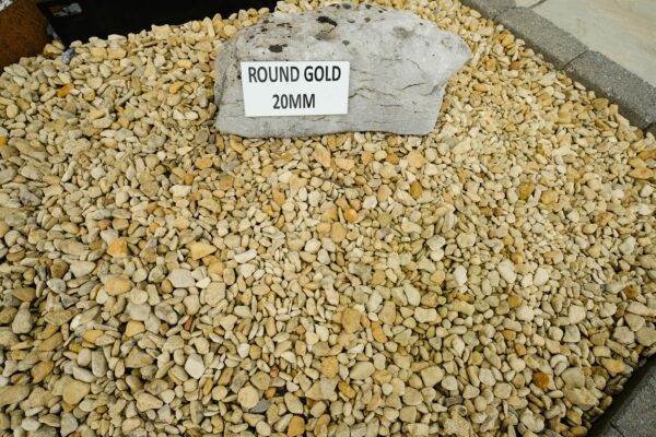 A large pile of round gold 20mm stones with a sign on a rock that reads 'ROUND GOLD 20MM'.