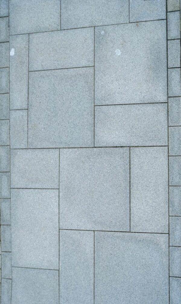 An assortment of gray, bush-hammered silver granite tiles on display, with a descriptive label affixed to the top right, various sizes of tiles neatly arranged next to a small section filled with smaller, multicolored pebbles.