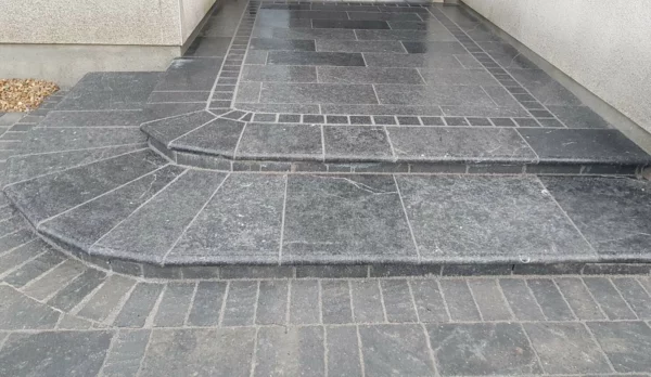 An accessible ramp and steps constructed from dark paving stones, demonstrating an integration of a sloped path and stairs for combined use.