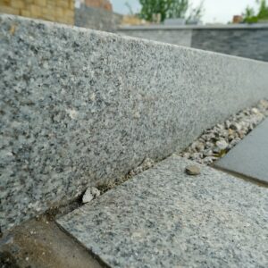 Close-up of a granite kerbstone and pavement with a blurred background of a stone wall.