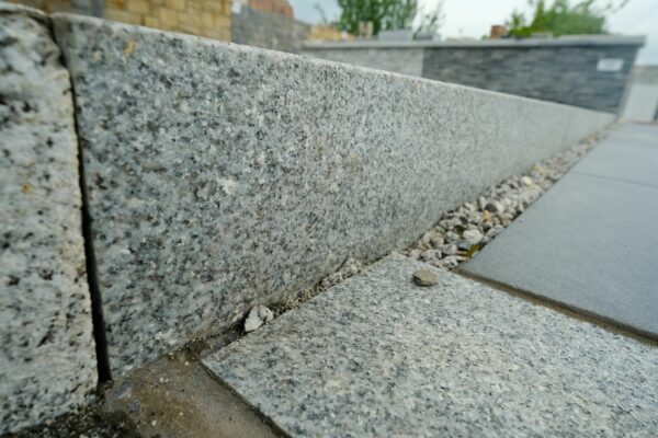 Close-up of a granite kerbstone and pavement with a blurred background of a stone wall.