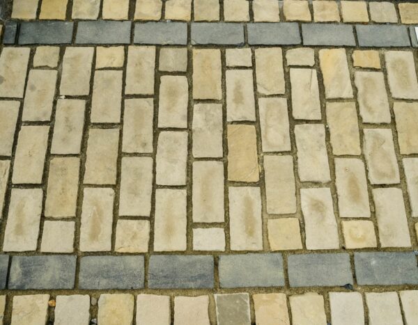 A patterned pavement showcasing a sample of black limestone cobbles bordered by rectangular stones on a bed of gravel.