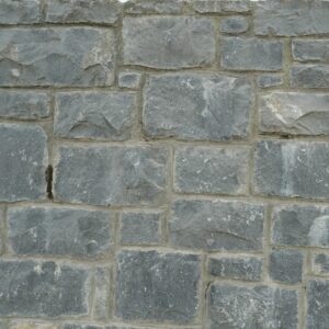 A close-up of a Headford stone wall featuring irregular-shaped grey stones with a sign indicating the stone type in the upper right corner.