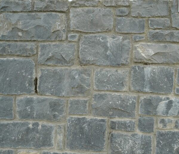 A close-up of a Headford stone wall featuring irregular-shaped grey stones with a sign indicating the stone type in the upper right corner.