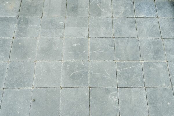 Alt text: A paved area with uniformly laid Kilkenny limestone slabs surrounded by pebbles, with a label on one slab indicating "Kilkenny Limestone 200x100 Tumbled Cobble."