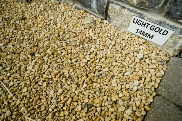 A pile of light gold-colored pebbles labeled "LIGHT GOLD 14MM" against a stone foundation.