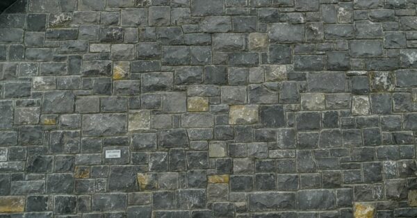 A stone facade on a building with a triangular gable and visible roof eaves, featuring a stone bench near steps on the right side.