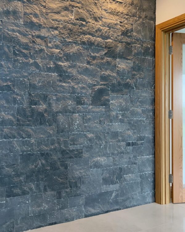 A textured gray stone wall with a wooden door frame on the right side, featuring a light reflection on the stone surface.