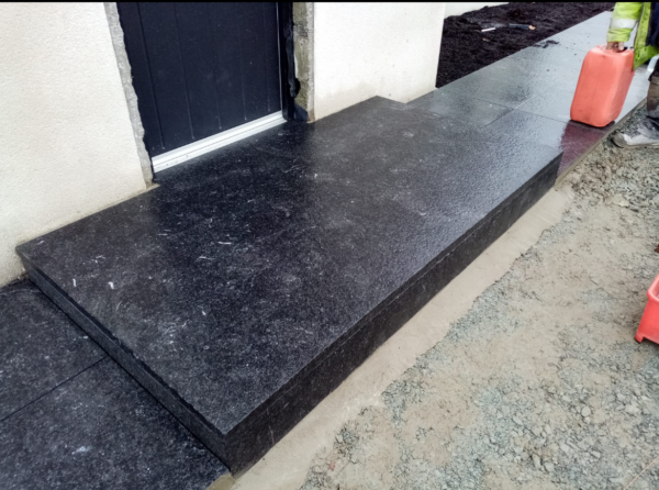 A black granite step leading up to a door, with construction materials and tools visible in the foreground.