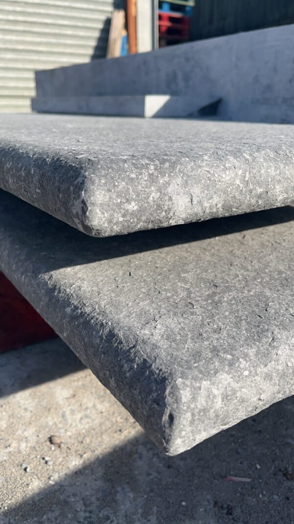 Close-up of stacked gray concrete slabs with a textured surface, set against a blurred background of a construction site.