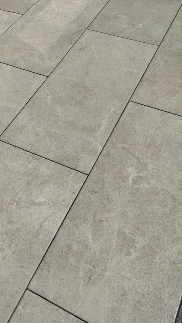 Close-up of light-colored textured tiles laid in a rectangular pattern, with visible grout lines between them.