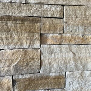 A close-up view of a textured stone wall made of various rectangular and irregularly shaped light-colored stones, displaying multiple shades of beige and gray.