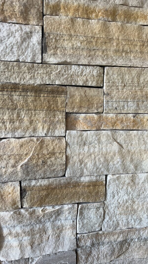 A close-up view of a textured stone wall made of various rectangular and irregularly shaped light-colored stones, displaying multiple shades of beige and gray.