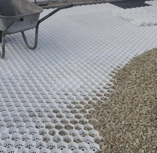 A wheelbarrow on a newly laid white hexagonal grid paving system, with a portion filled with gravel to the side.