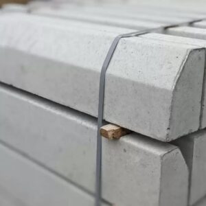 Bundled concrete slabs stacked on a pallet, secured with gray straps, with a small wooden block visible between them.