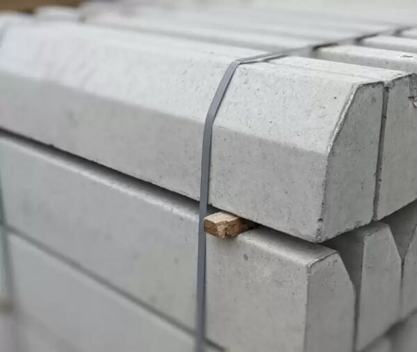 Bundled concrete slabs stacked on a pallet, secured with gray straps, with a small wooden block visible between them.