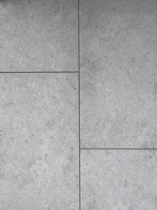 A close-up view of large, light gray stone tiles arranged in a grid pattern, featuring subtle variations in texture and color.