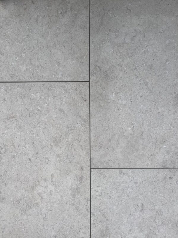 A close-up view of large, light gray stone tiles arranged in a grid pattern, featuring subtle variations in texture and color.