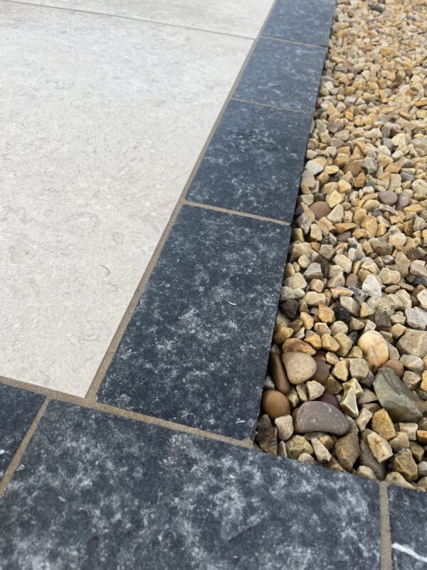 Close-up of a paving surface featuring light-colored and dark-colored tiles, with a border of small pebbles along the edge.