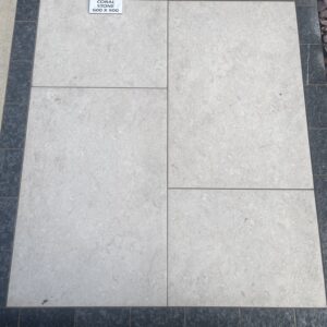 A surface of light-colored coral stone tiles, measuring 600 x 900, bordered by dark gray stone tiles, with small pebbles visible in the background.