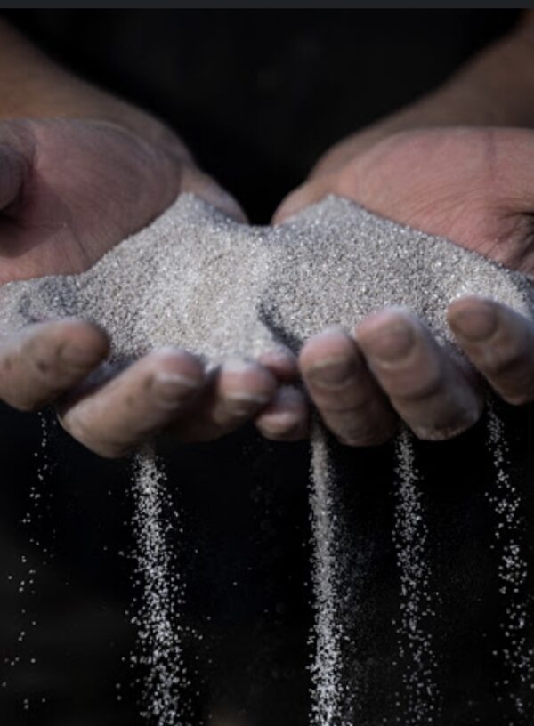 Two hands are holding a mound of fine sand, with some grains cascading down from between the fingers against a dark background.