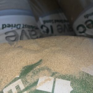 A close-up of a pile of fine sand with a partially obscured green bag in the background, featuring white text.