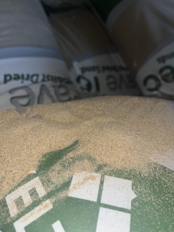 A close-up of a pile of fine sand with a partially obscured green bag in the background, featuring white text.