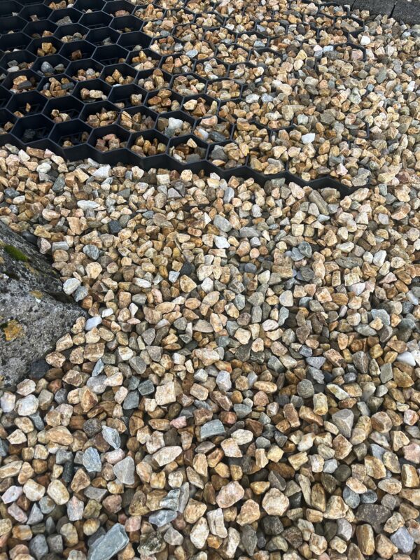 Close-up view of a mix of small, colorful stones scattered over a surface, with a section featuring hexagonal black plastic grid underneath some of the stones.