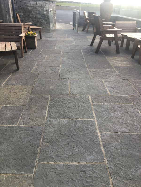 A stone-paved courtyard with wooden benches and a planter of flowers, leading to a glass-paneled entrance.